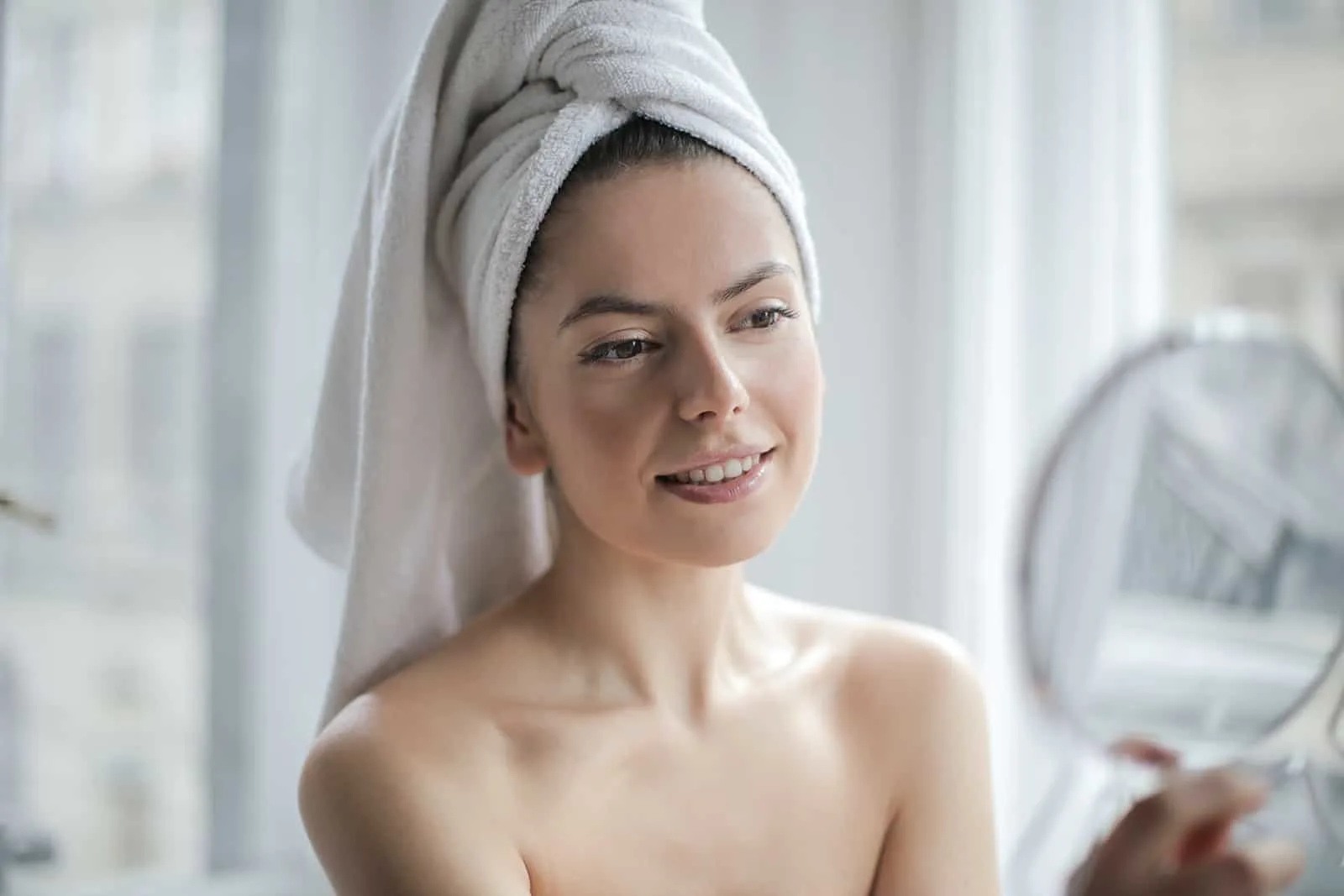 eine Frau mit einem Handtuch auf dem Kopf, die einen Spiegel hält und sich selbst ansieht