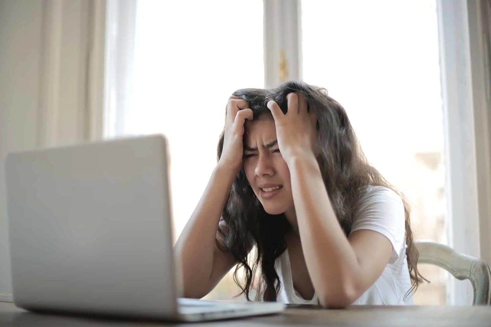 Eine gestresste Frau sitzt vor einem Laptop und berührt die Haare mit den Händen