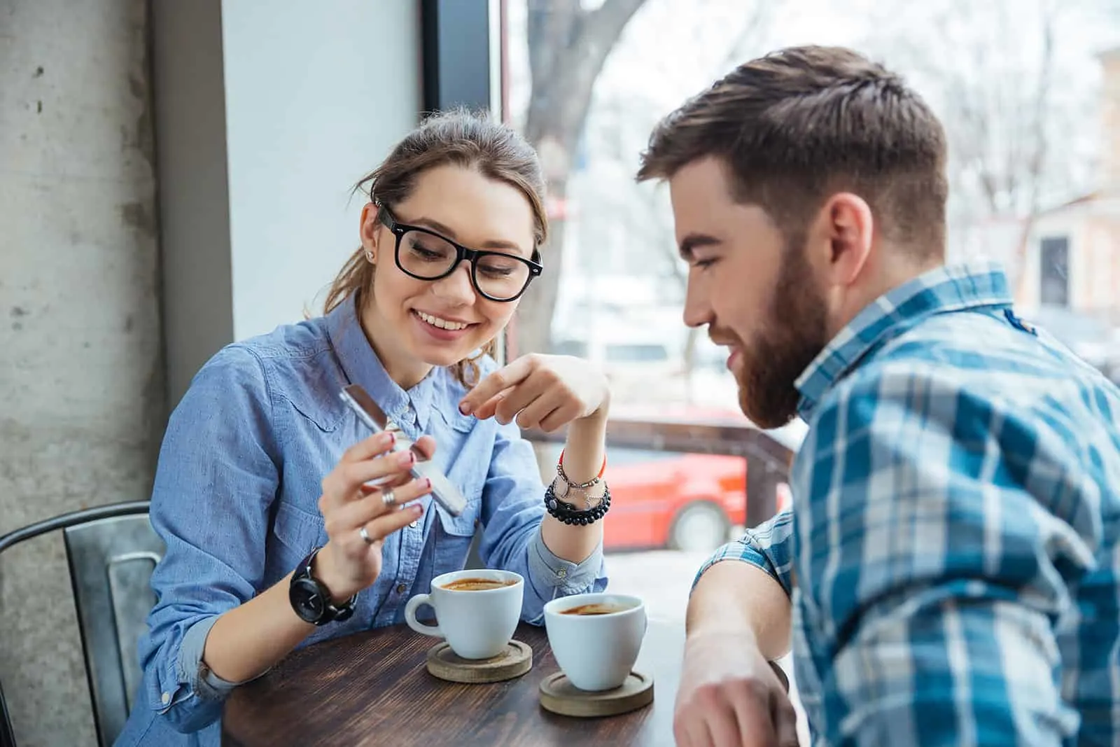 Eine lächelnde Frau zeigt einem Mann, der mit ihr im Café sitzt, ein Smartphone