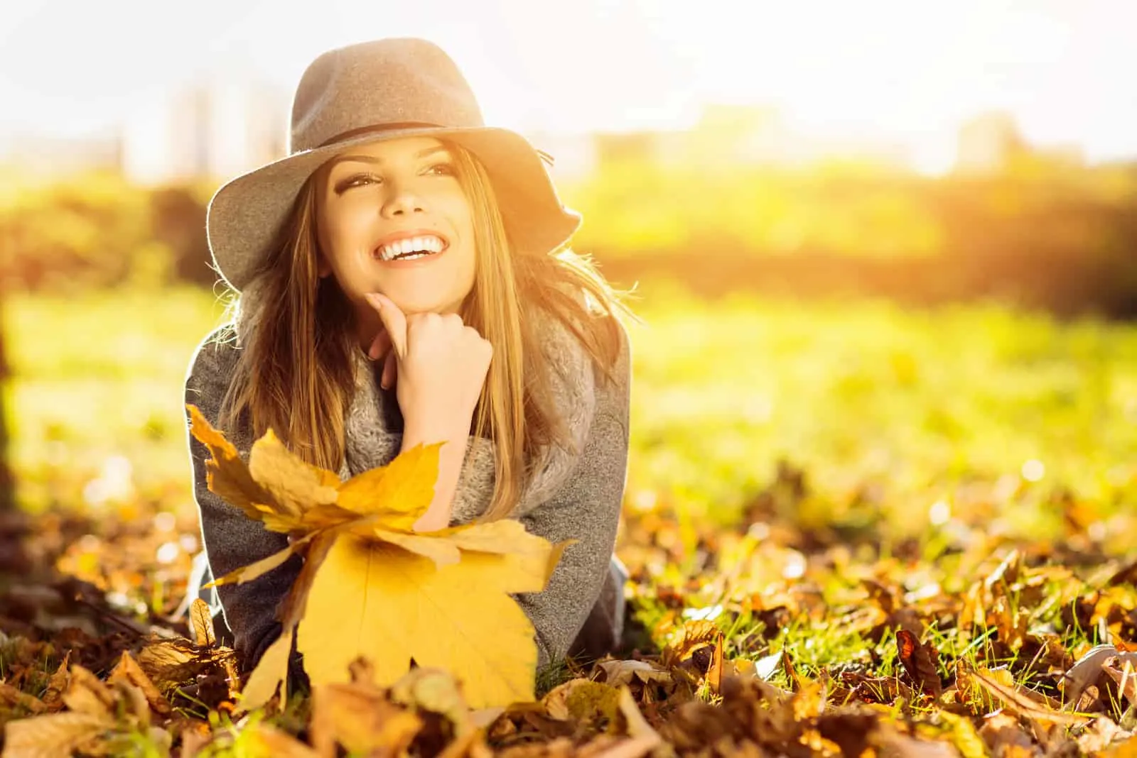eine lächelnde Frau, die im Herbst auf einem Blatt liegt