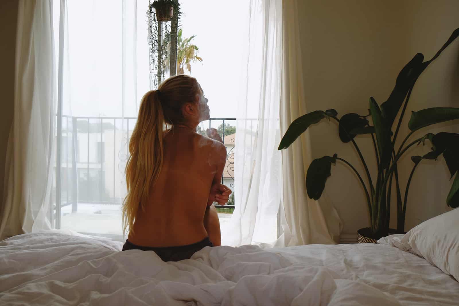 eine toplesse Frau, die auf der Bettkante sitzt und nachdenkt
