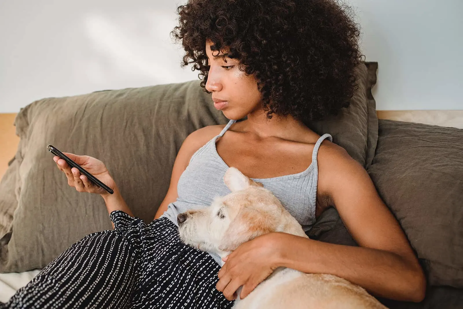 ernsthafte Frau, die ein Smartphone beim Sitzen auf der Couch mit einem Hund betrachtet