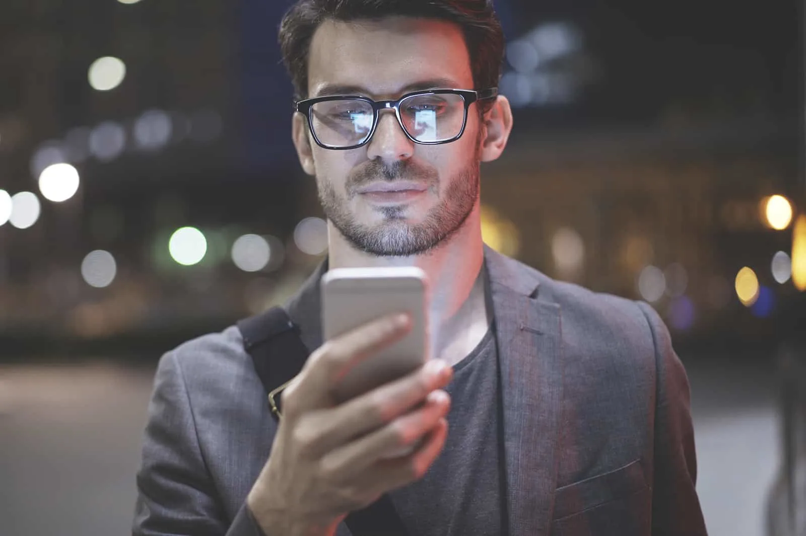 lächelnder Mann, der Smartphone betrachtet, während er nachts draußen steht