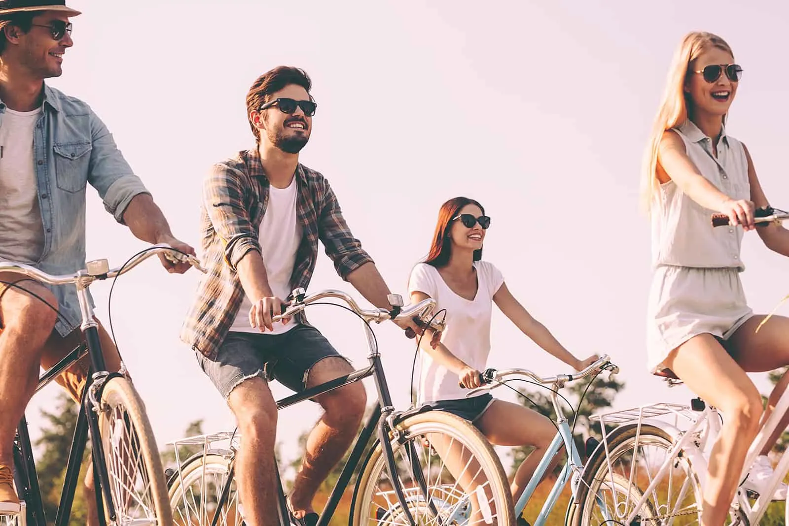 vier fröhliche Freunde, die an einem sonnigen Tag Fahrrad fahren