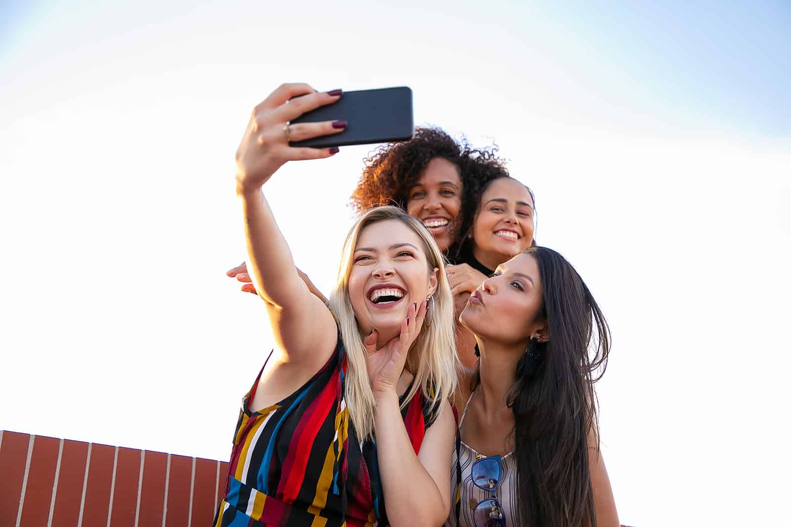 vier lächelnde Freundinnen, die beim Abhängen ein Selfie machen