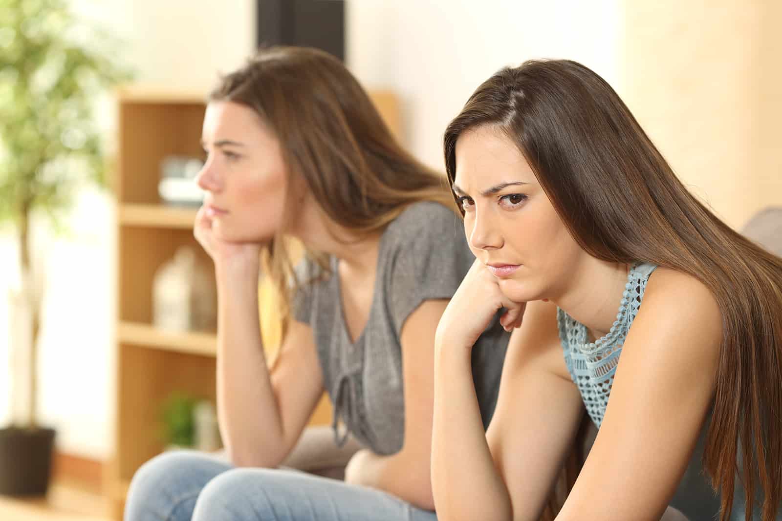wütende Frau dreht den Kopf von ihrer Freundin, die auf dem Sofa sitzt