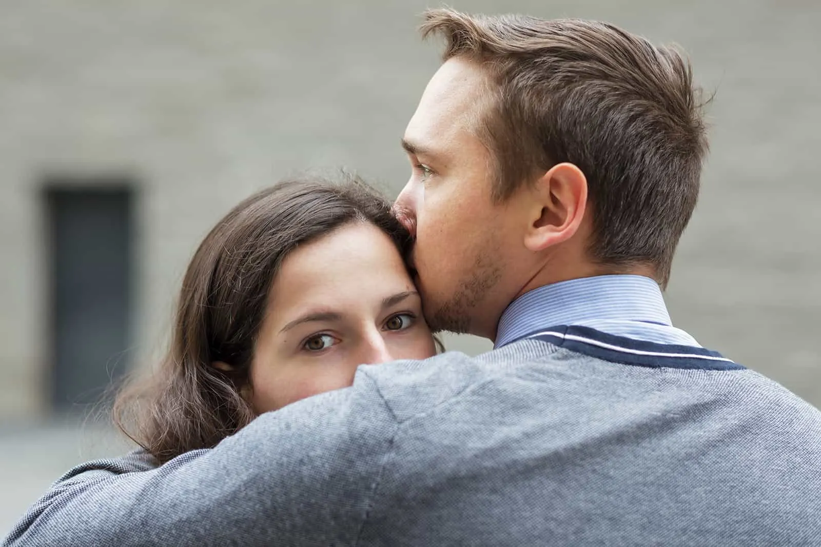 Ein Mann küsst eine Frau auf die Stirn, während sie zur Seite schaut