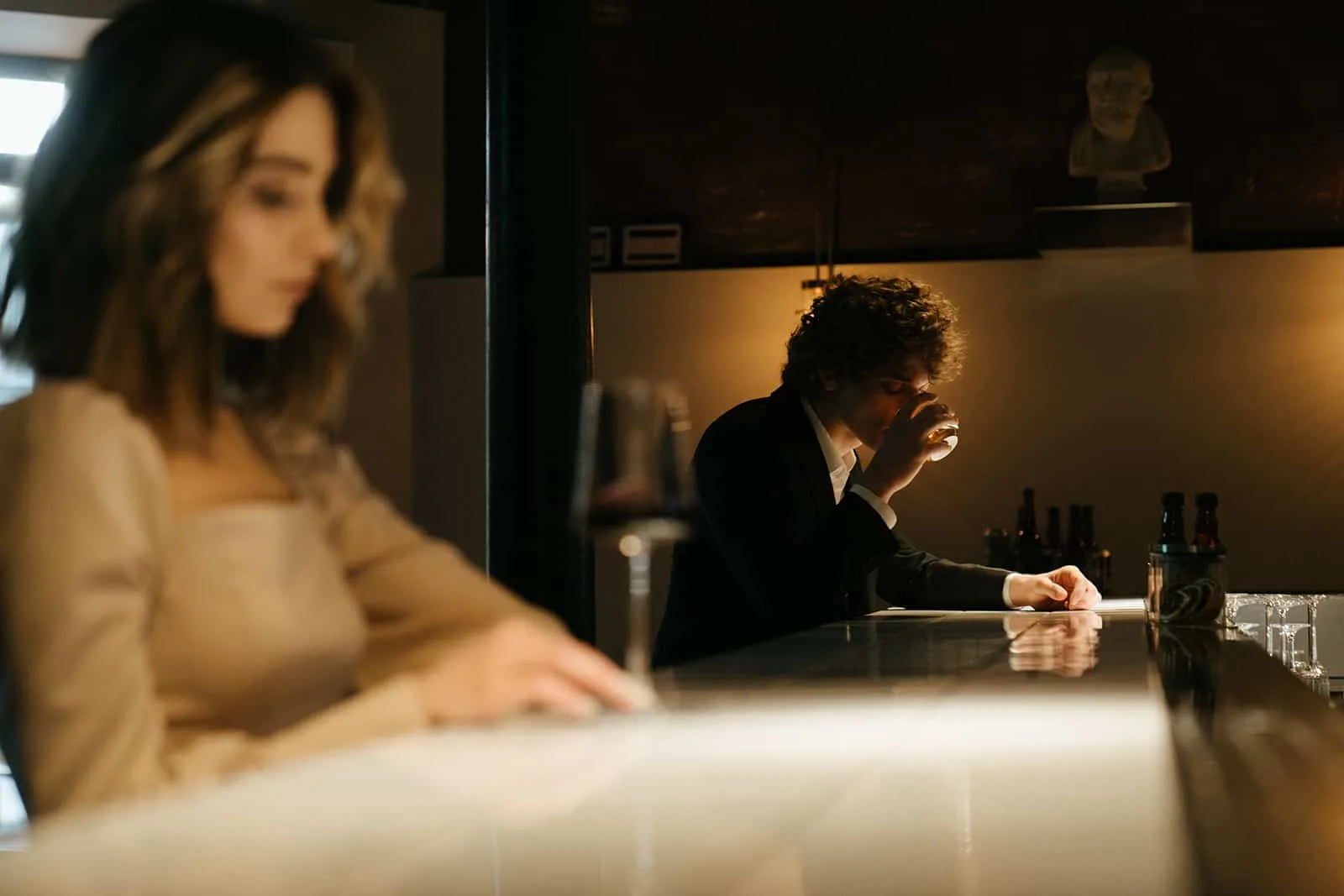 Ein Mann sitzt alleine an der Theke und trinkt aus dem Glas in der Nähe einer Frau