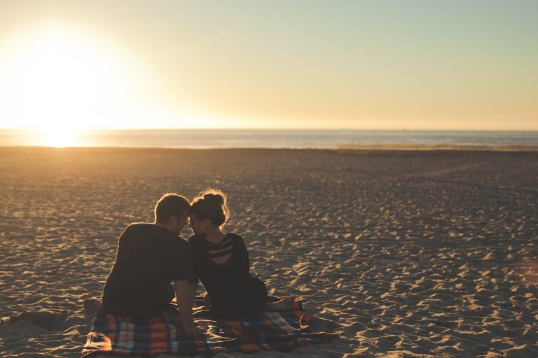 ein Mann und eine Frau sitzen am Strand während des Sonnenuntergangs