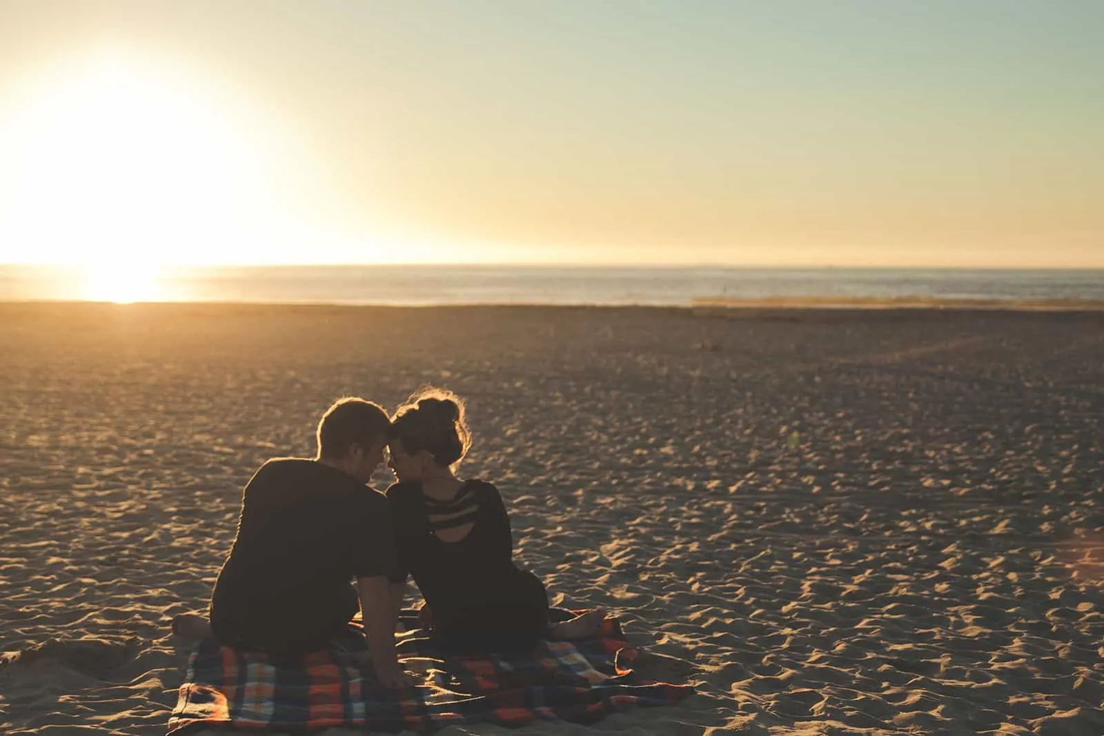 ein Mann und eine Frau sitzen am Strand während des Sonnenuntergangs
