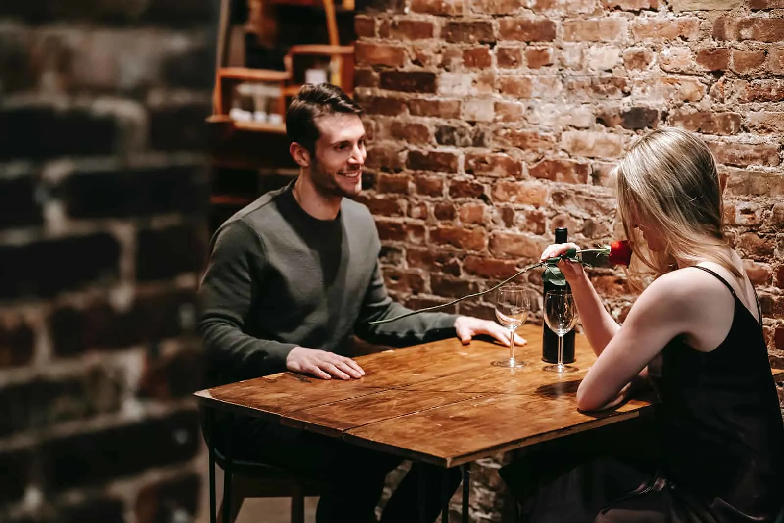 Ein lächelnder Mann, der elegante Frau betrachtet, die mit ihm im Restaurant sitzt und Rose riecht