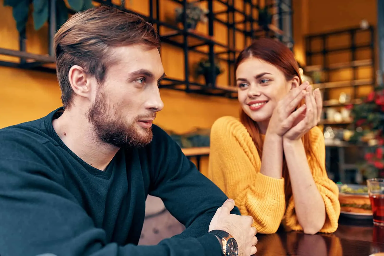 eine lächelnde Frau, die einen attraktiven Mann betrachtet, während sie zusammen im Café sitzen