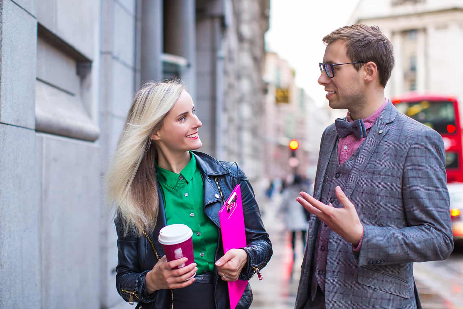 eine lächelnde Frau, die ihrem schick gekleideten männlichen Kollegen zuhört, während sie zusammen auf der Straße gehen