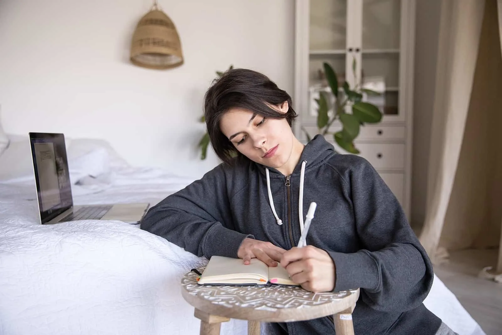 eine nachdenkliche Frau, die in ein Notizbuch schreibt, während sie in der Nähe des Bettes sitzt