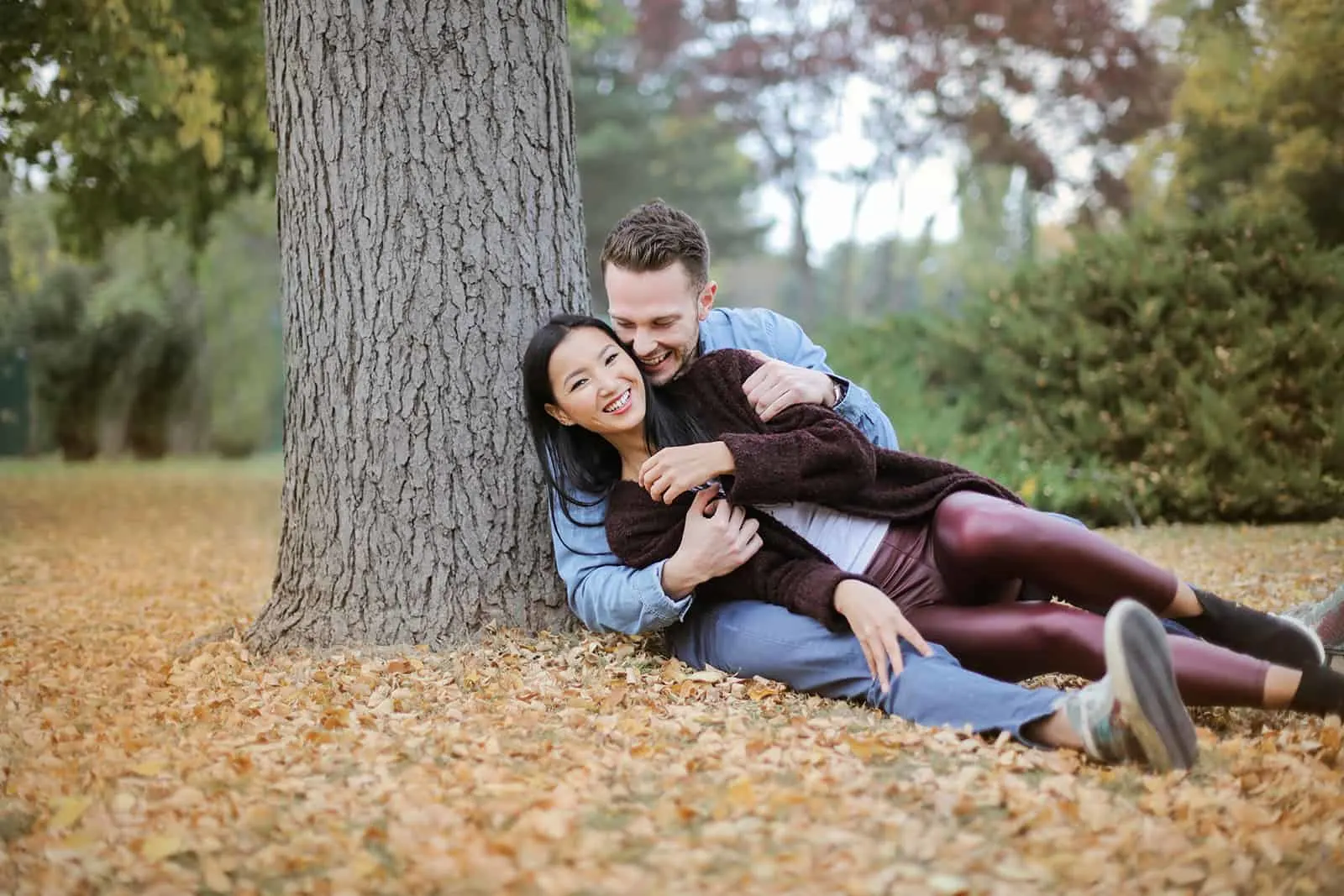 lächelndes Paar sitzt auf den getrockneten Blättern und kuschelt