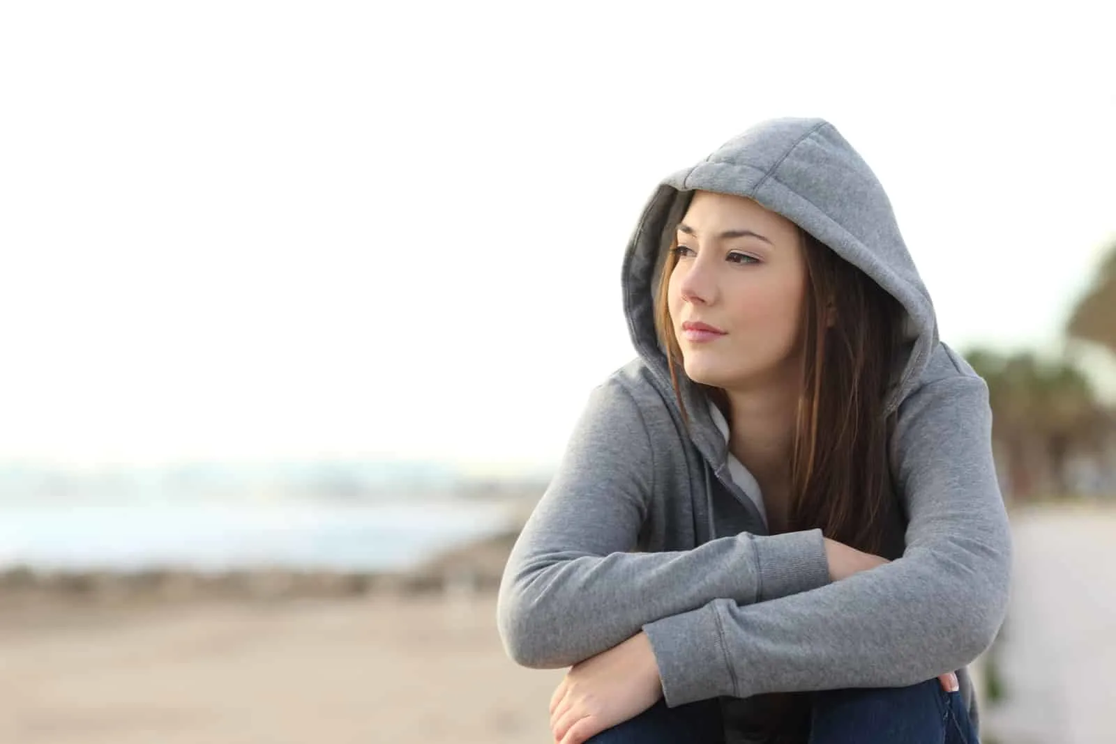 nachdenklicher Teenager sitzt am Strand und schaut weg