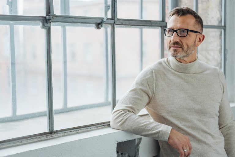 Mann der eine Brille trägt, die durch Fenster steht