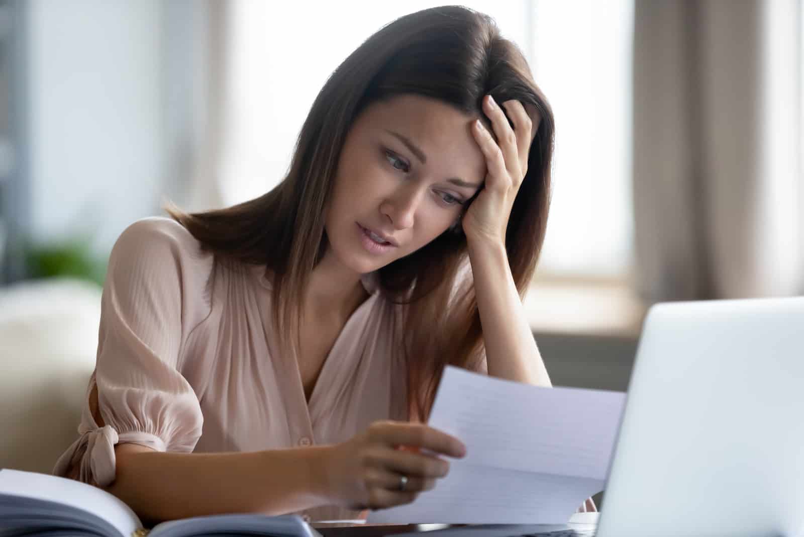 Eine Frau, die an einem Laptop sitzt, liest einen Brief und weint