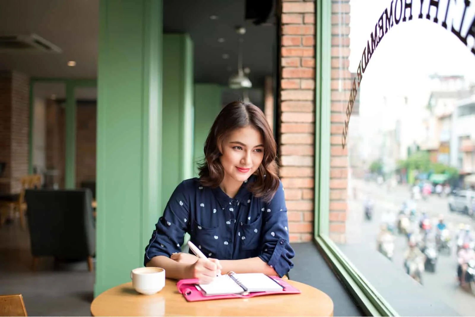 Eine Frau, die mit Kaffee an einem Tisch sitzt, schreibt
