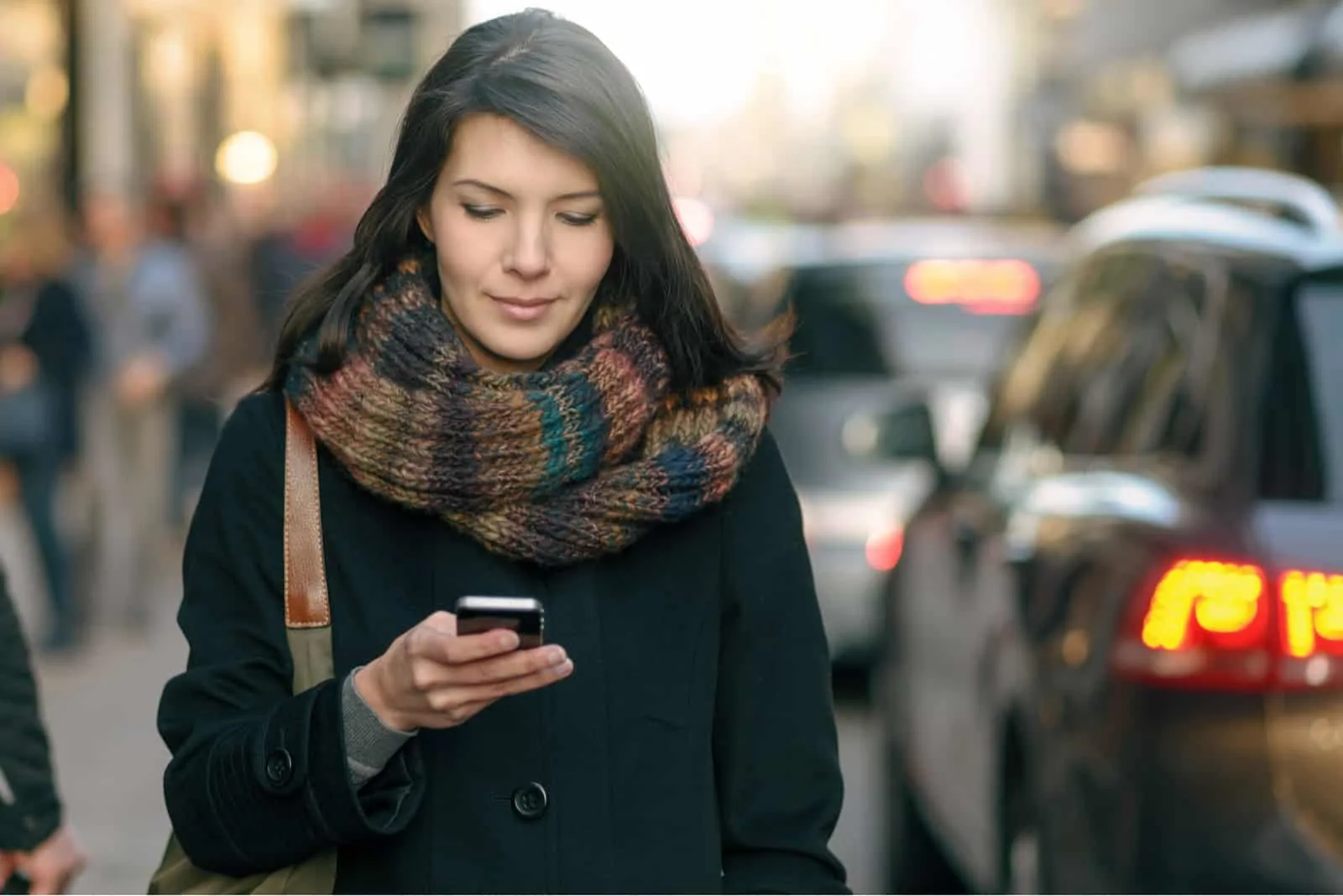 Eine Frau in einem schwarzen Mantel geht die Straße entlang und sendet eine SMS auf ihr Smartphone