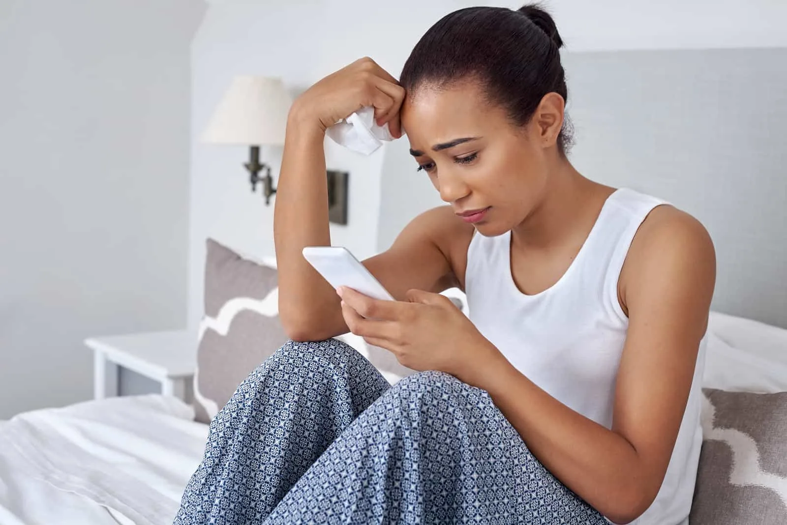 Eine traurige Frau im Bett benutzt ein Handy