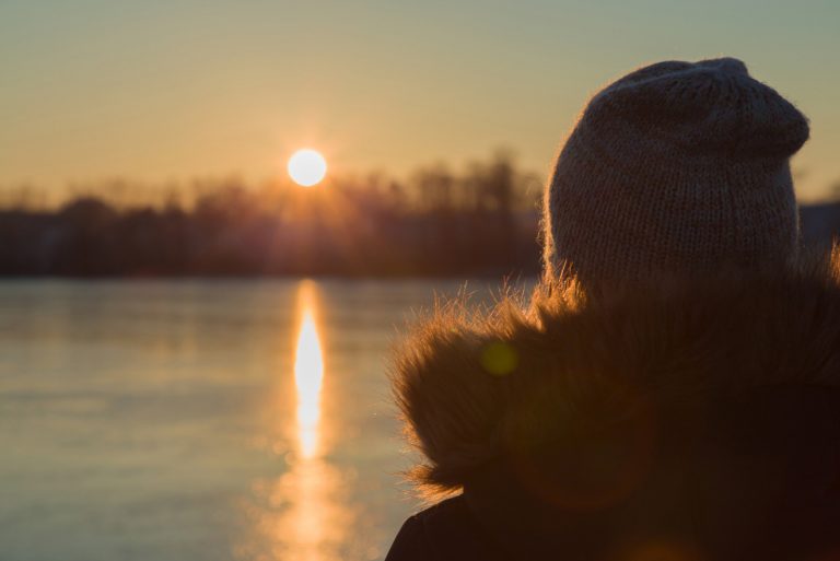 Junge erwachsene Frau, die allein steht und auf orange gelben Sonnenuntergang starrt