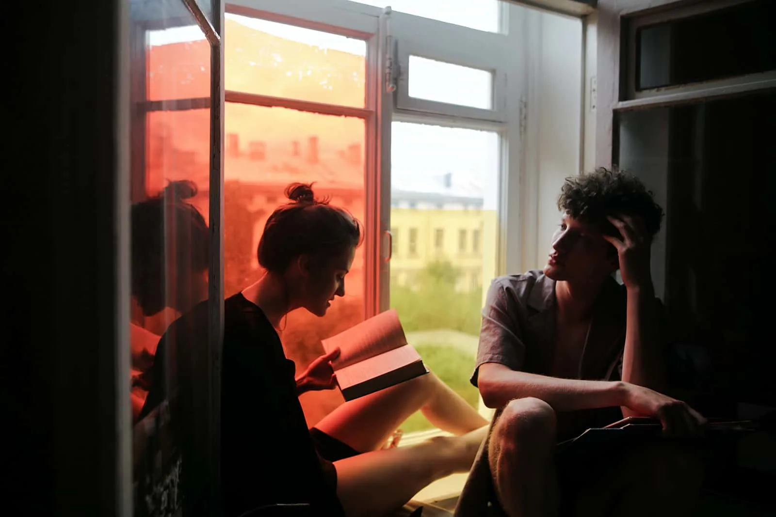 eine Frau, die einem Mann ein Buch vorliest, während sie zusammen auf einer Fensterbank sitzt