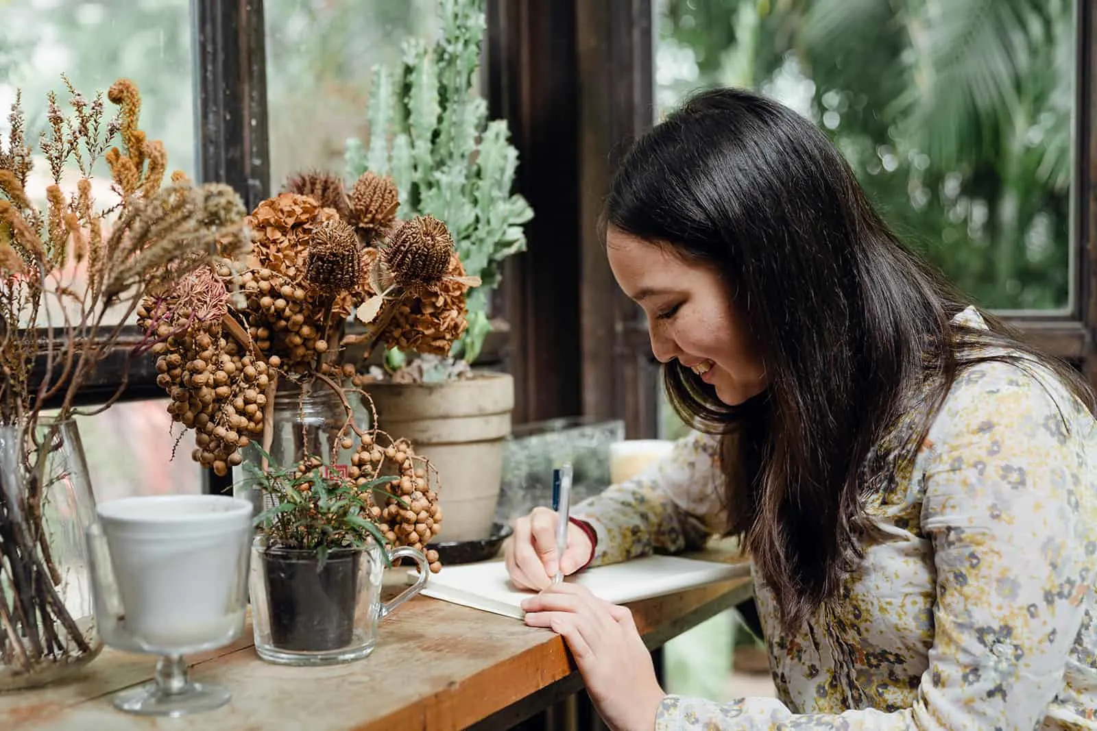 eine glückliche Frau, die einen Liebesbrief schreibt, während sie in der Nähe der Pflanzen sitzt