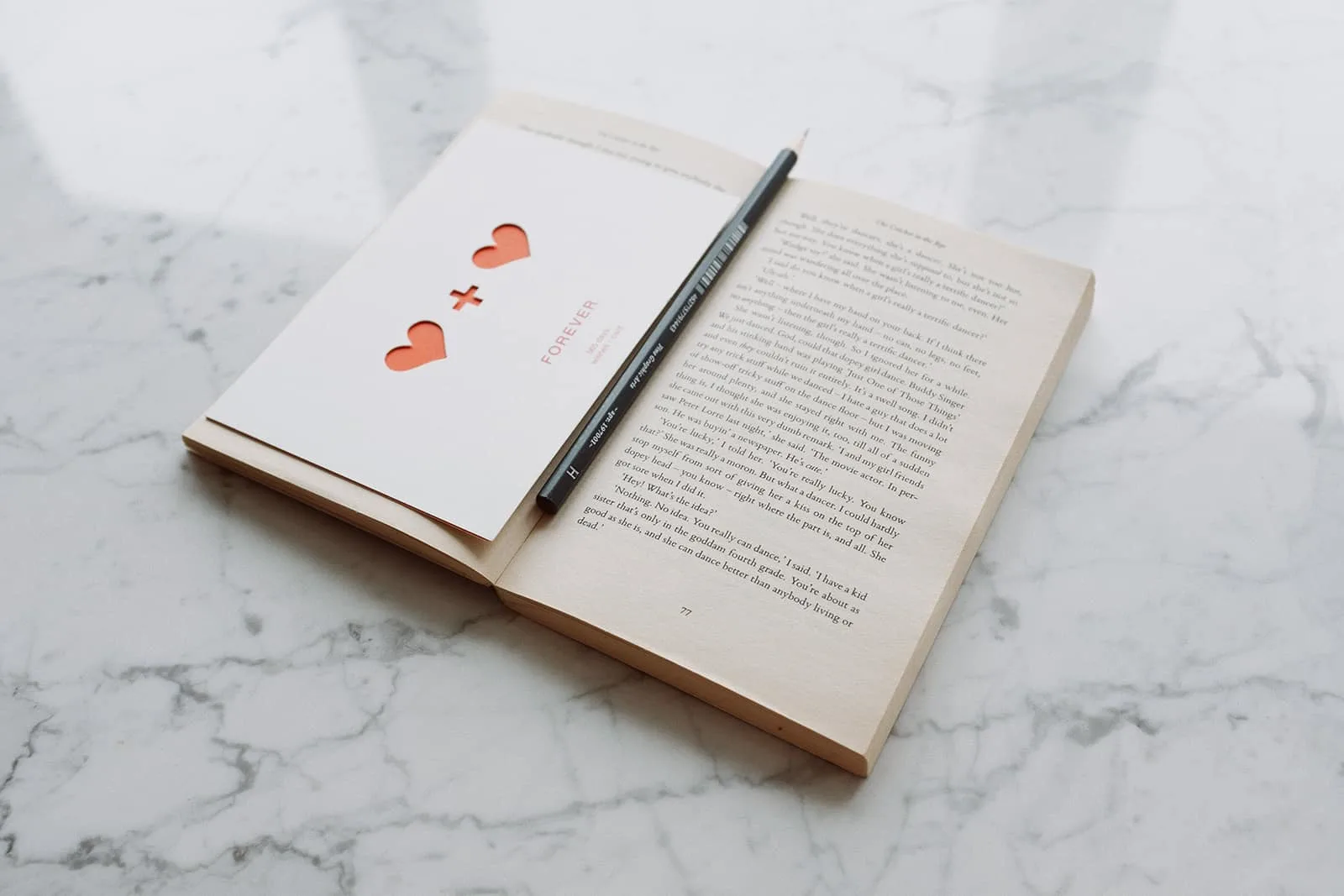 geöffnetes Buch mit Bleistift und Liebespostkarte auf Marmoroberfläche