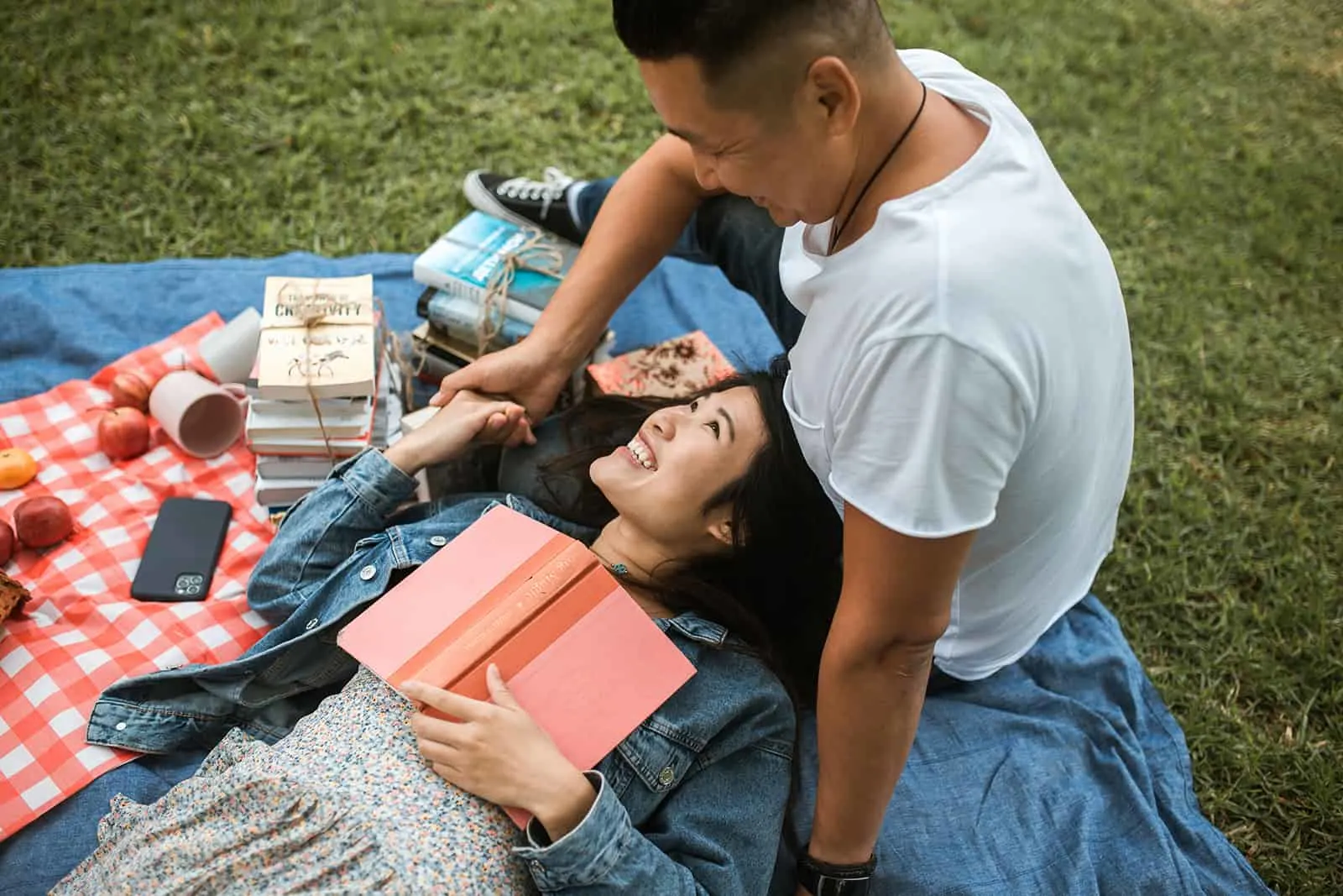glückliche Frau, die ein Buch hält und ihren Freund beim Liegen auf der Decke beim Picknick ansieht