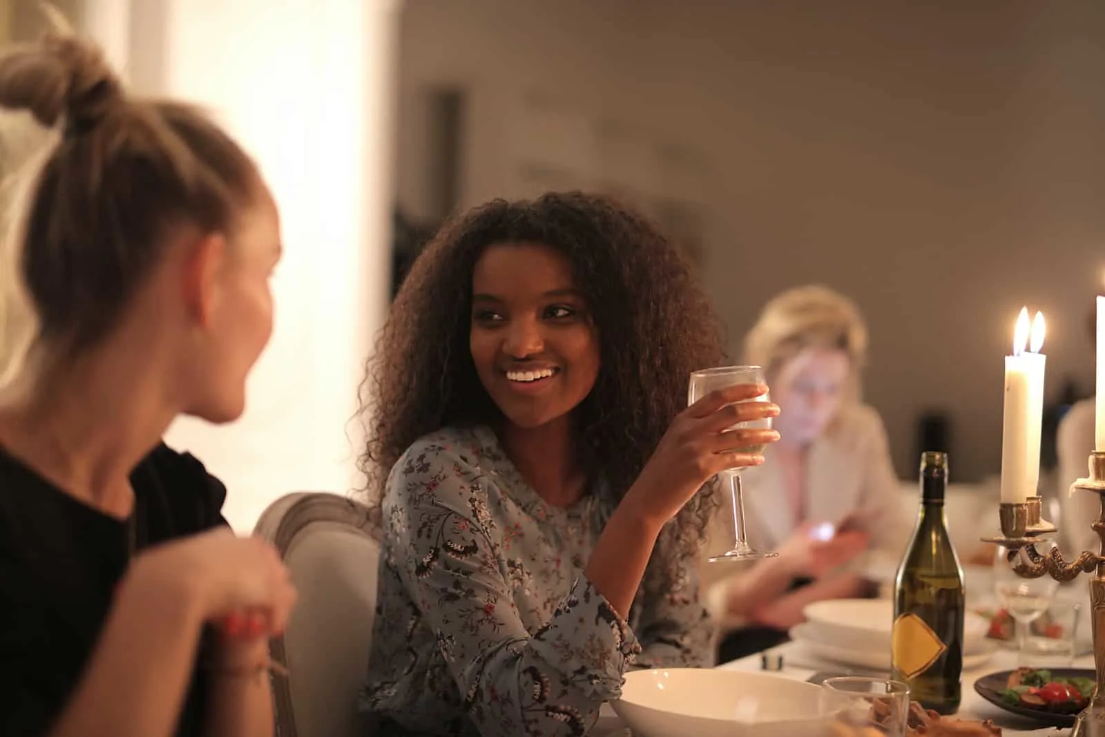lächelnde Frau, die Wein hält und mit einer Freundin während eines Abendessens spricht