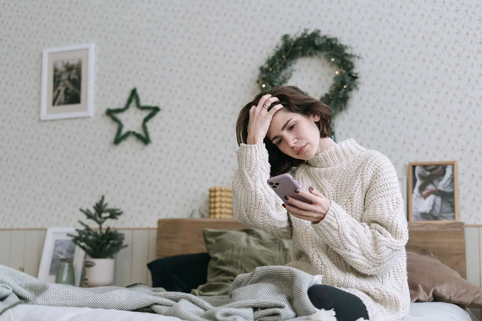 traurige Frau, die Smartphone beim Sitzen auf dem Bett betrachtet