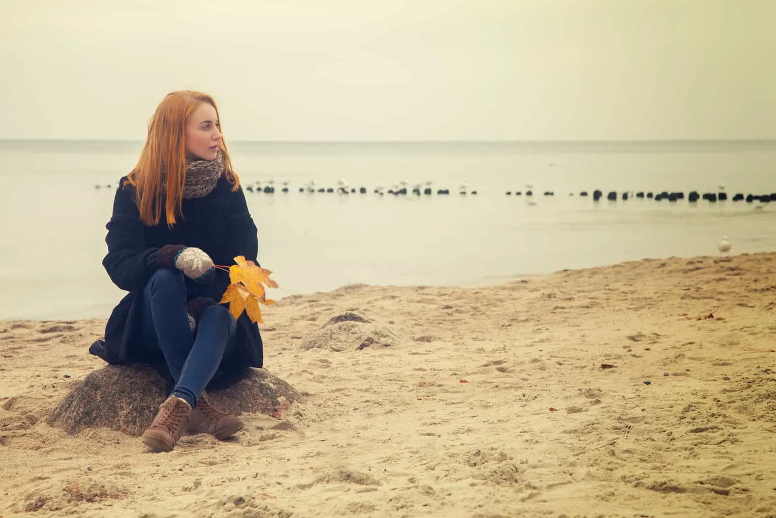 traurige nachdenkliche Frau am herbstlichen Meeresstrand sitzend