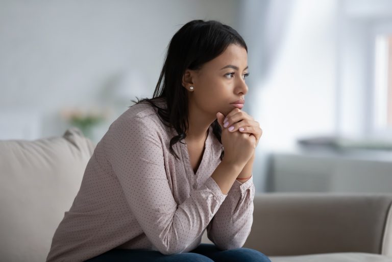 Frau sitzt auf dem Sofa im Wohnzimmer und denkt an das Problem