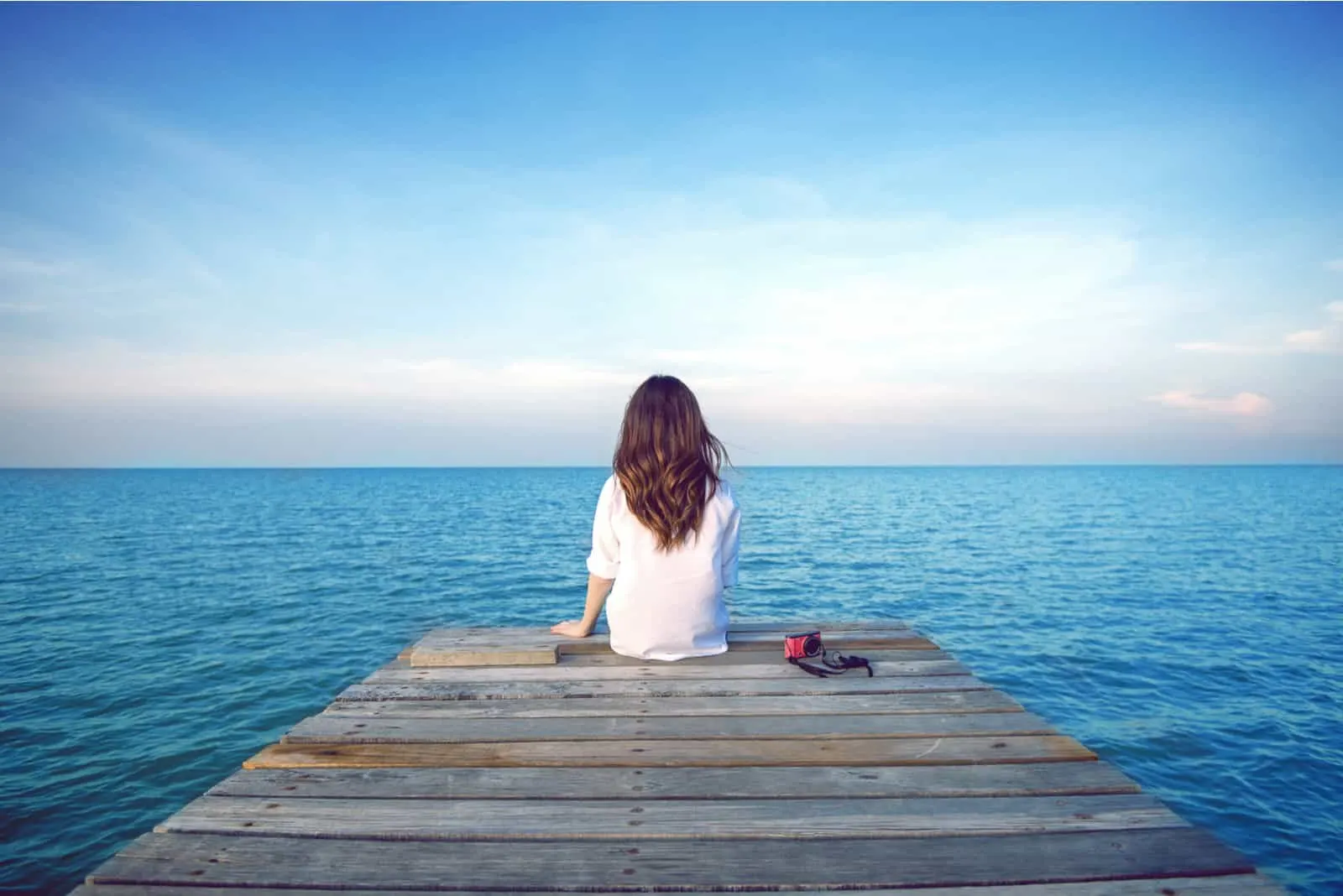 Eine imaginäre Frau sitzt auf einem Pier und schaut auf das Meer