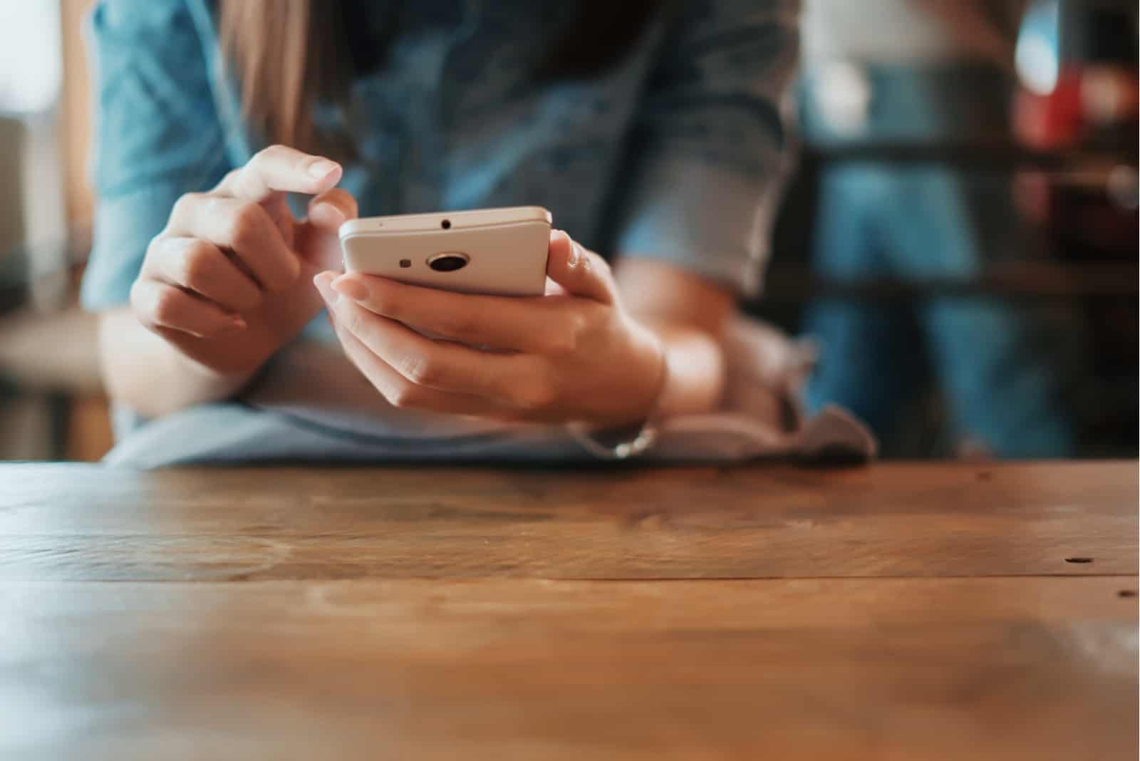 Hand der Frau, die Smartphone auf Holztisch verwendet