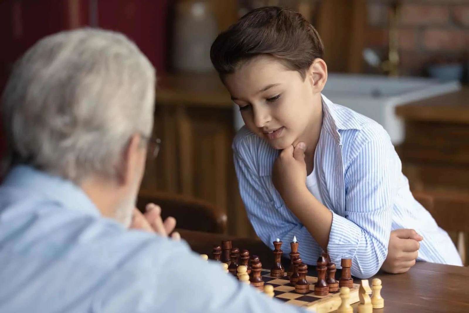 Junge Kind spielen Schach mit alten 60er grauhaarigen Großvater
