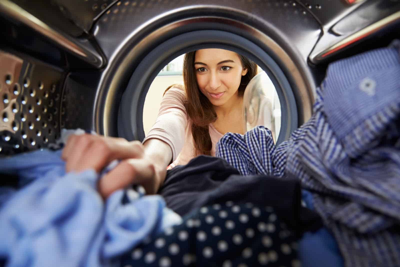 Frau, die Wäsche tut, die innerhalb der Waschmaschine erreicht