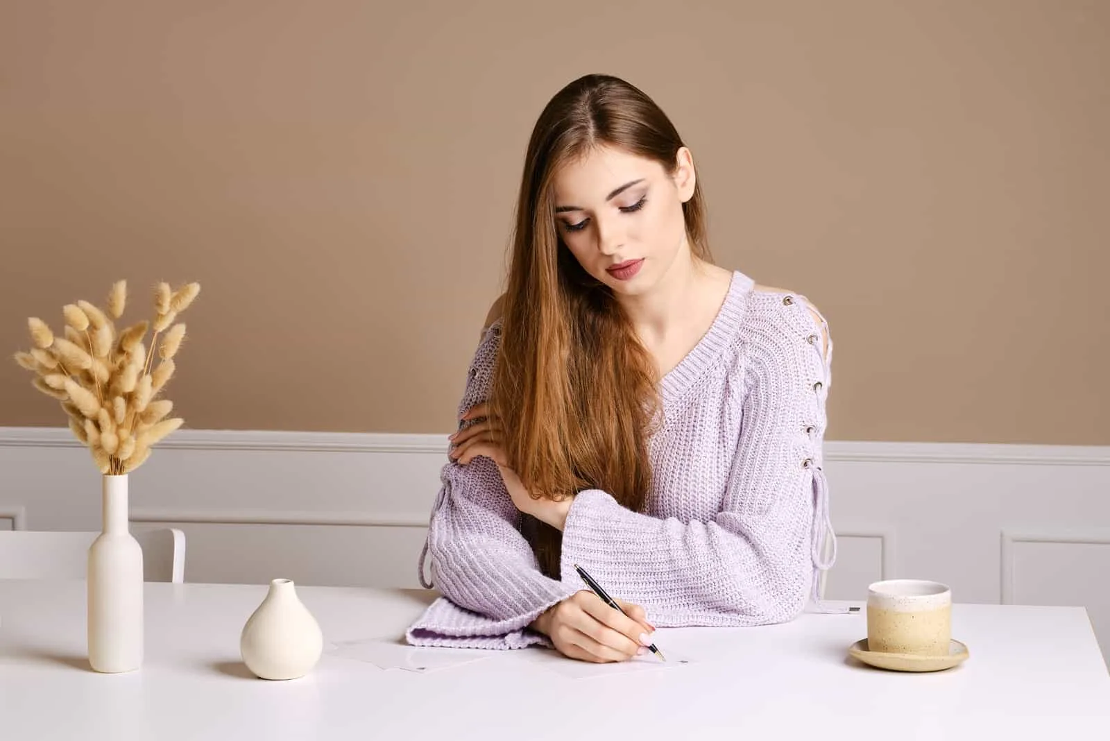 Frau mit langen braunen Haaren sitzt am Tisch und schreibt Gruß