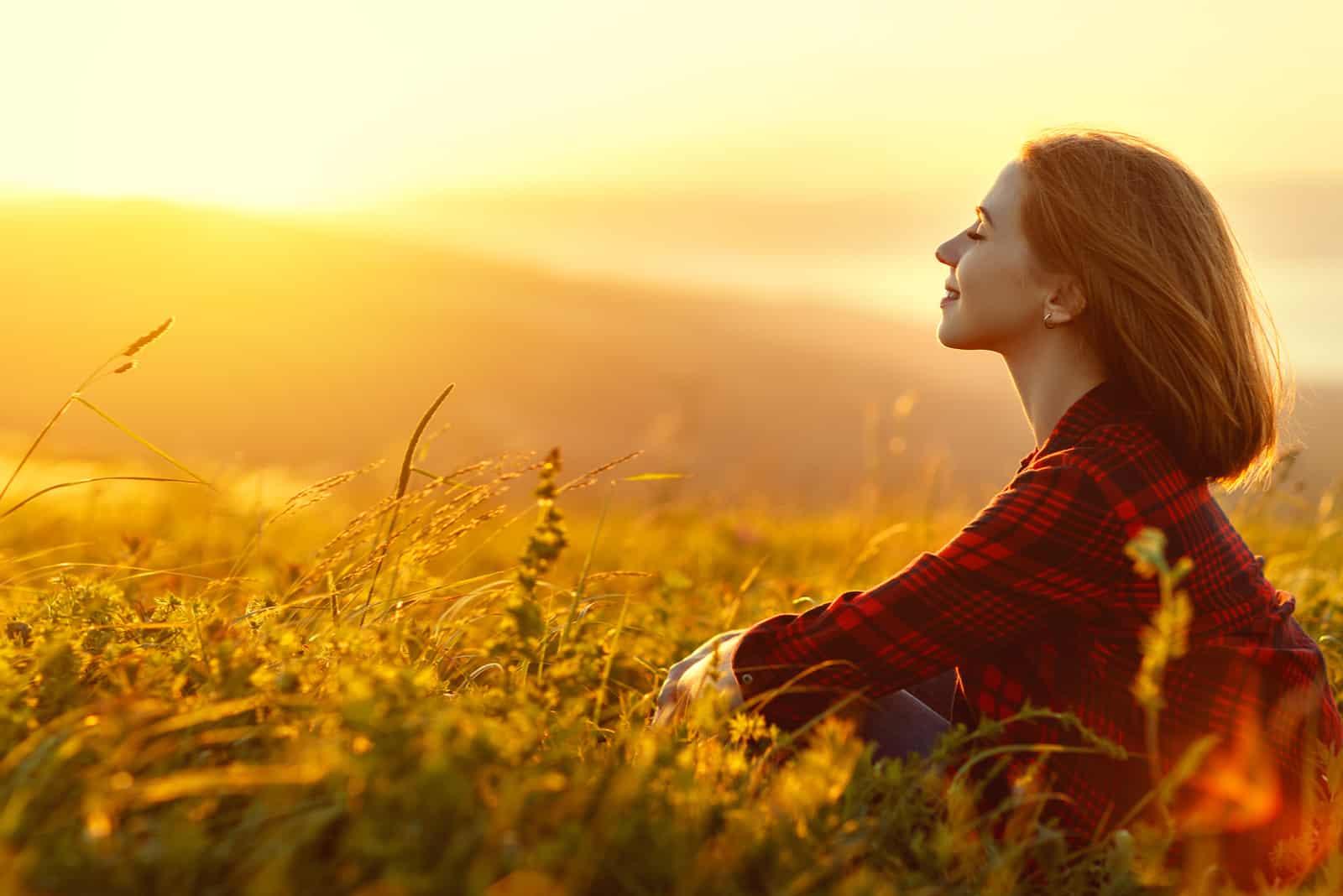Frau sitzt mit dem Rücken auf dem Feld und bewundert den Sonnenuntergang