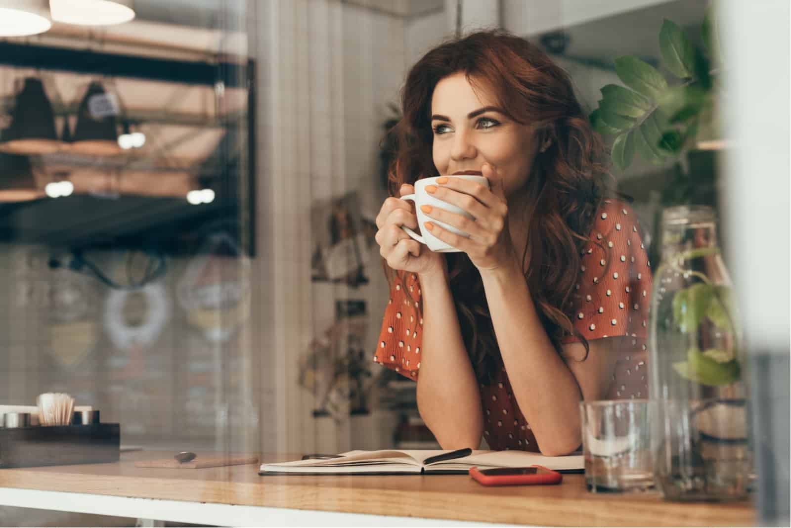 junge Frau, die Kaffee am Tisch mit Notizbuch im Café trinkt