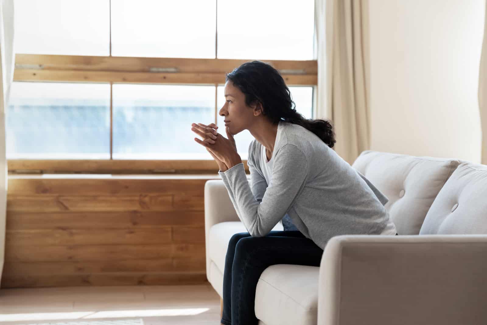 junge Frau, die auf gemütlicher Couch ruht und in die Ferne schaut