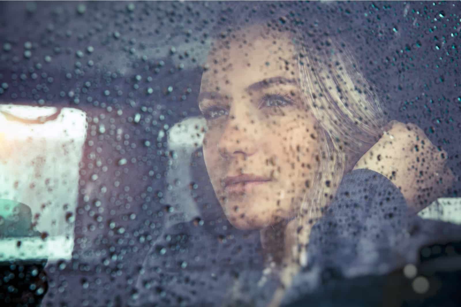 traurige Frau, die im Auto bei Regenwetter sitzt