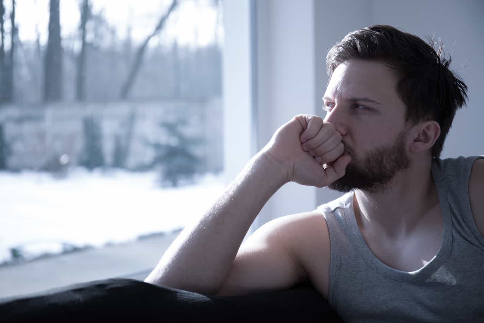 unglücklicher gutaussehender Mann, der am Fenster sitzt
