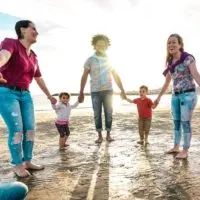 Standpunkt einer glücklichen Familie, die am Strand Hand in Hand gegen den Sonnenuntergang spielt