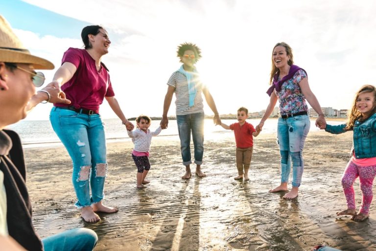 Standpunkt einer glücklichen Familie, die am Strand Hand in Hand gegen den Sonnenuntergang spielt