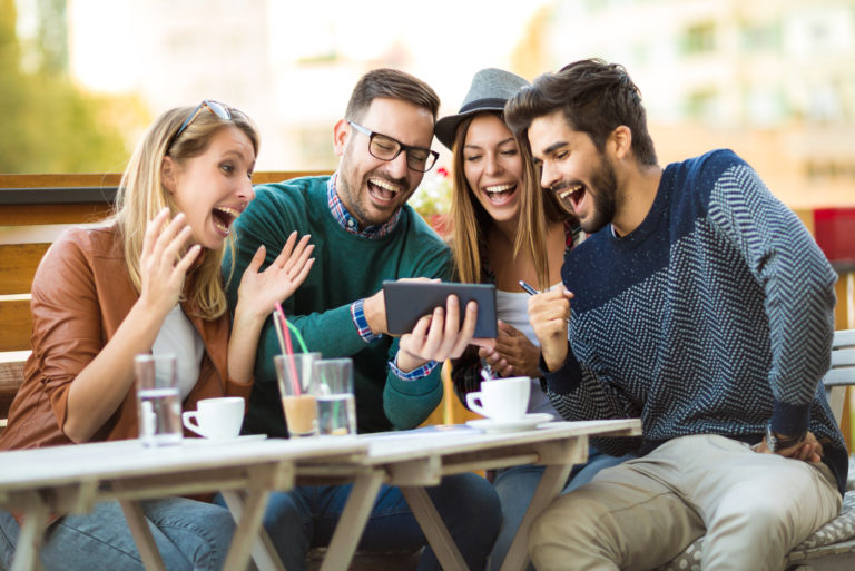 Freunde sitzen da und schauen sich etwas auf dem Tablet an und lachen