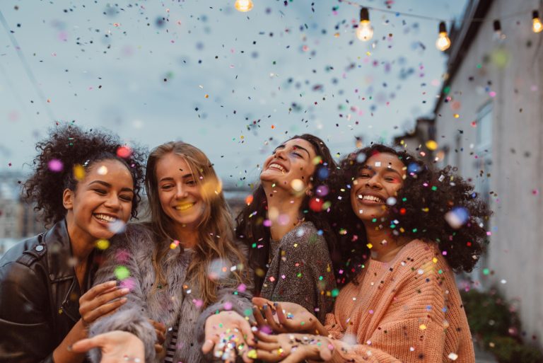 Vier schöne Frauen stehen auf einer Terrasse unter Konfetti