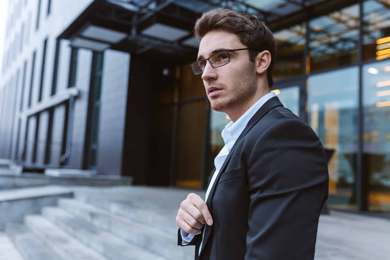 Geschäftsmann in Anzug und Brille seitlich stehend