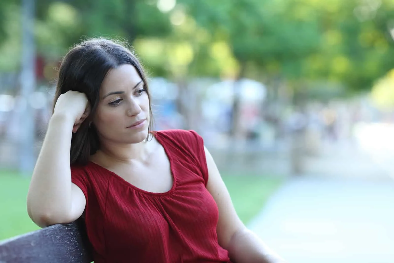 Nachdenkliche Frau sitzt auf einer Bank in einem Park und schaut weg